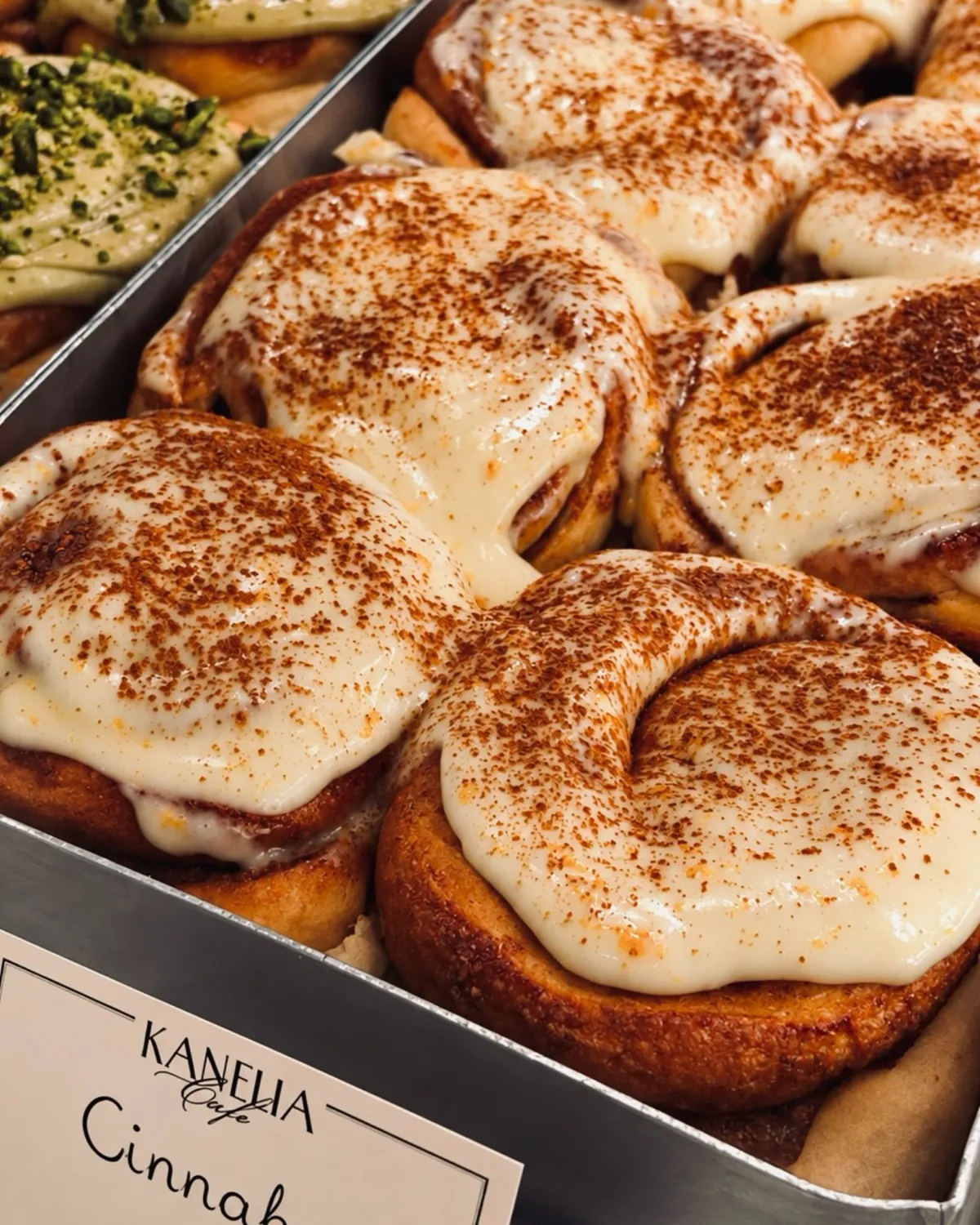 Kanēļmaizītes ar baltu glazūru un kanēli metāla formā ar Kanelia Cafe etiķeti